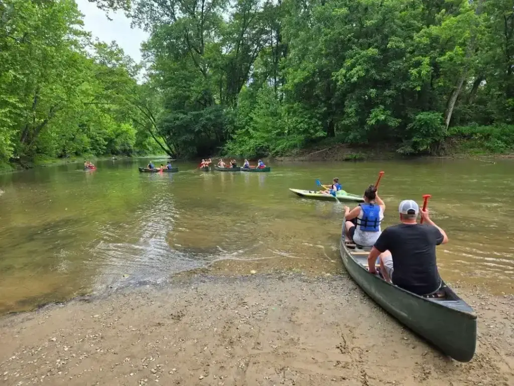 Paddlers pushing off from a sandbar on the Hocking River with other canoes ahead